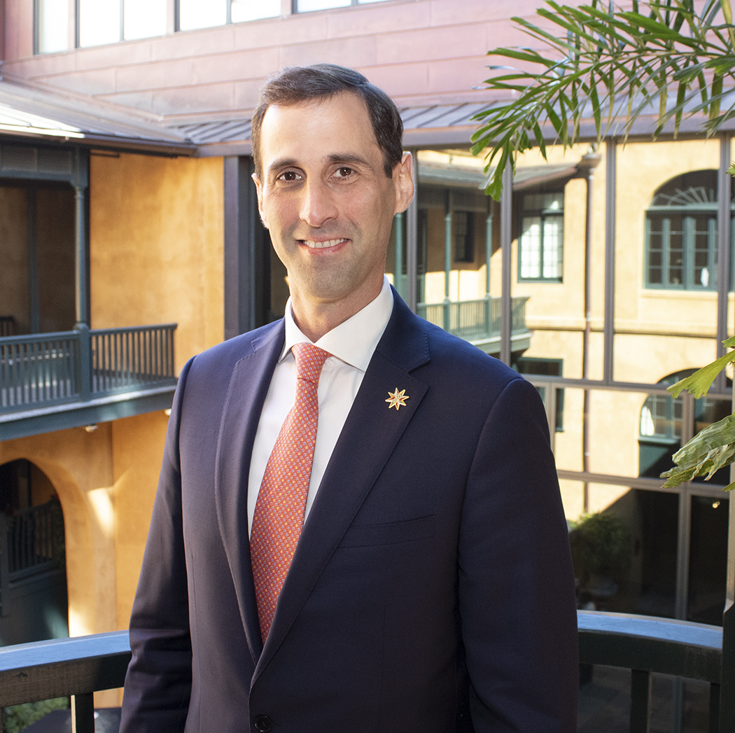 A headshot of Daniel Hammer, President and CEO of the Historic New Orleans Collection. The museum's courtyard can be seen in the background.