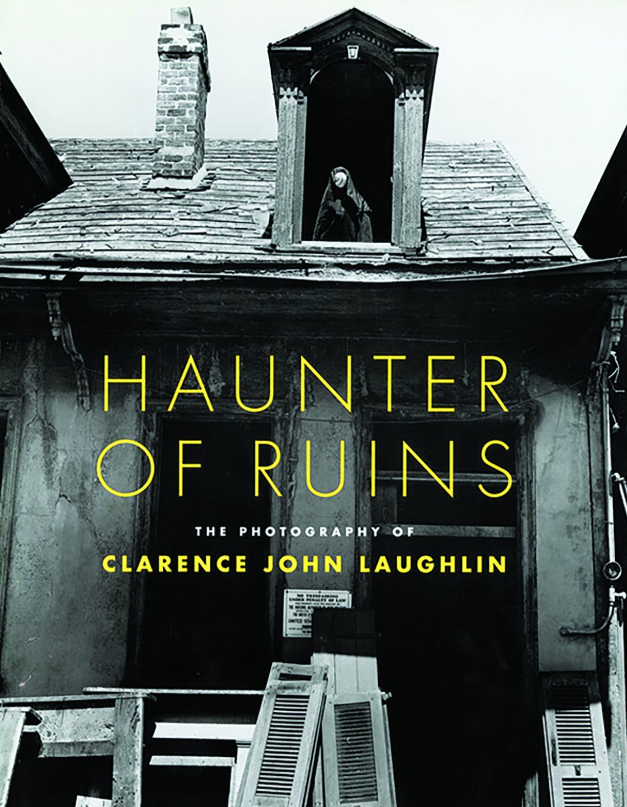 A black and white image of a dilapidated house with a figure in the attic window. The text reads Haunter of Ruins: The Photography of Clarence John Laughlin. There are broken shutters in the foreground.