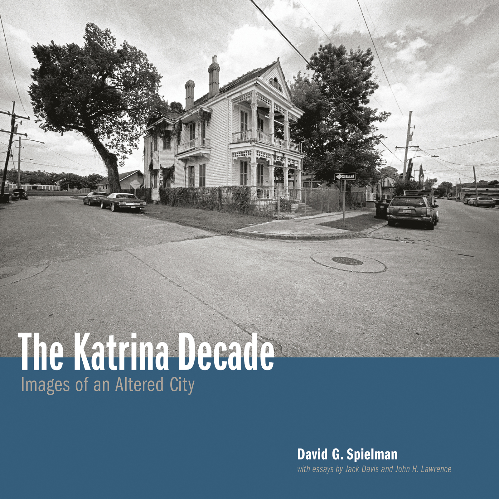 Black and white photo of a historic house at a street corner, surrounded by trees and power lines. The image is on the cover of a book titled The Katrina Decade: Images of an Altered City by David G. Spielman.