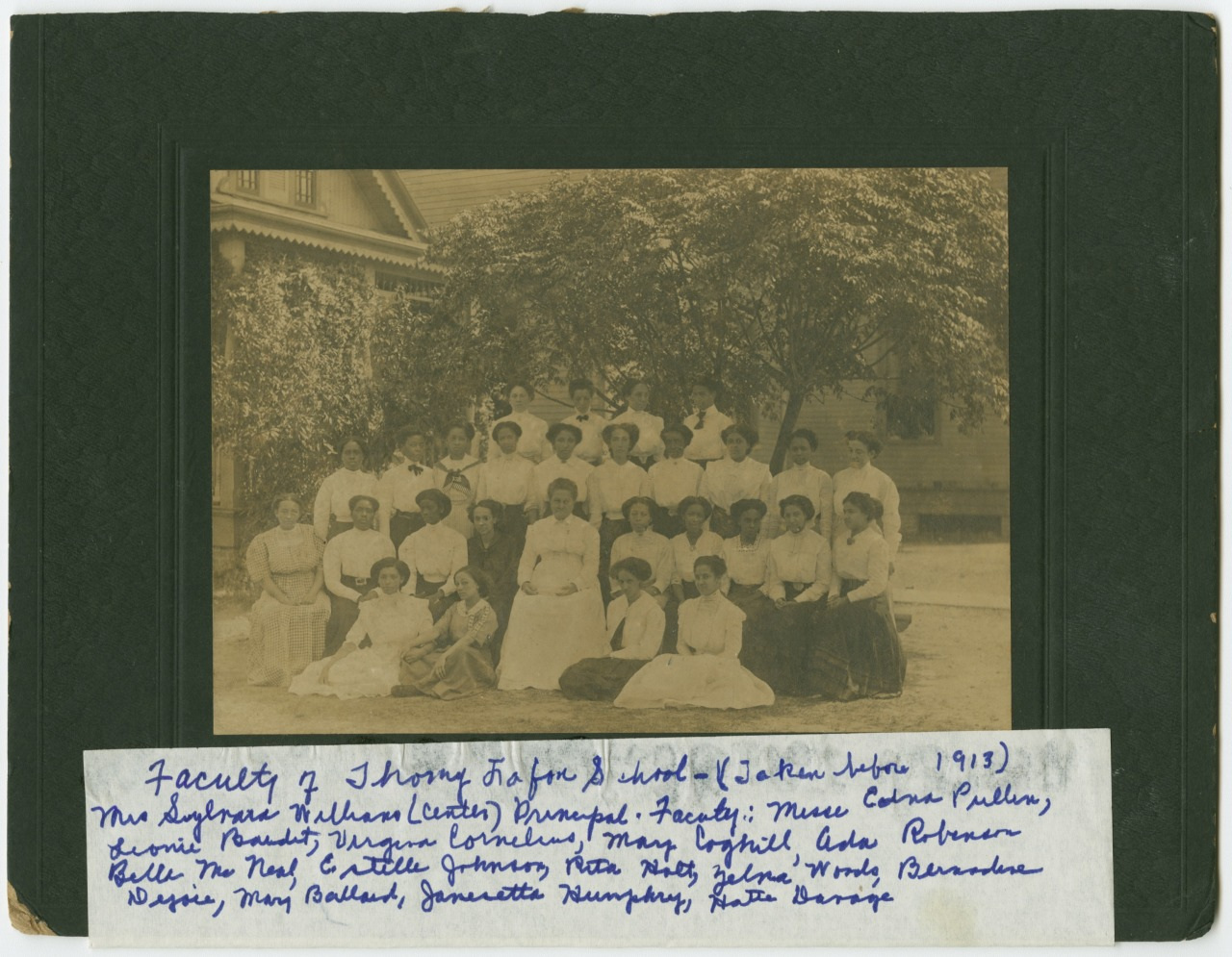 A sepia-toned photograph of a school faculty group from 1913. The large group of men and women is posing outdoors in front of trees. Handwritten notes below identify the photo as Faculty of Tuskegee Institute School along with several names.