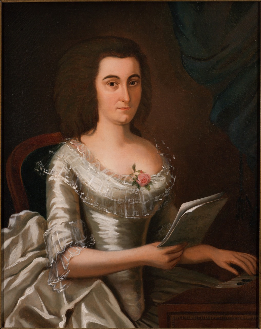 A historical painting of a woman in an elegant white dress with lace detailing, seated and holding a sheet of paper. A pink rose adorns her dress, and a dark curtain is visible in the background. Her expression is calm and composed.