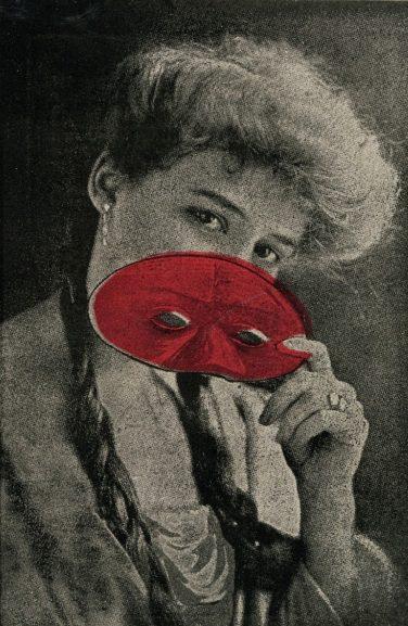 A woman holds a red mask partially covering her face, revealing her eyes. She has light-colored, voluminous hair and wears an elegant outfit with a ring on her finger. The image is in black and white except for the red mask.
