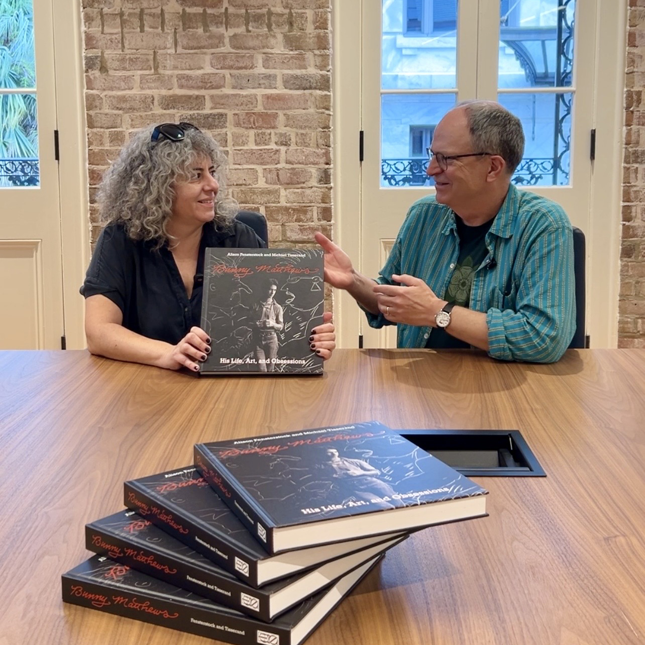Authors Michael Tisserand and Allison Fensterstock sit at a table signing copies of their book "Bunny Matthews: His Life, Art, and Obsessions."