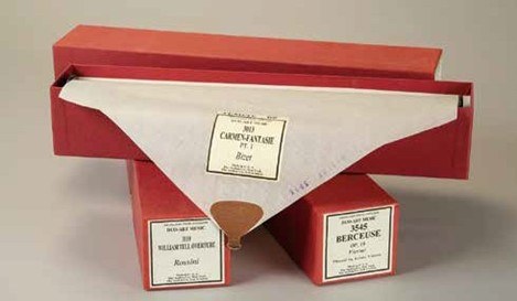 A vintage music box and piano roll titled Cachemfantasie Pt. 1 - Berei in a red box. Two additional rolls, Wellensittichmarsch and Berceuse, are displayed below in similar red boxes.