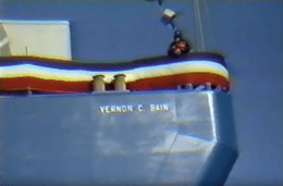 A screenshot from a vintage color film shows part of a ship with the name "VERNON C. BAIN" written on the side.
