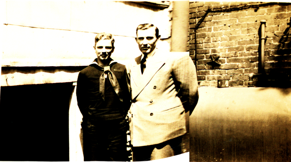 A man in a Navy uniform (Harold Shilke) standing next to a man in a suit (Boyd Cruise), with a brick wall visible behind them.
