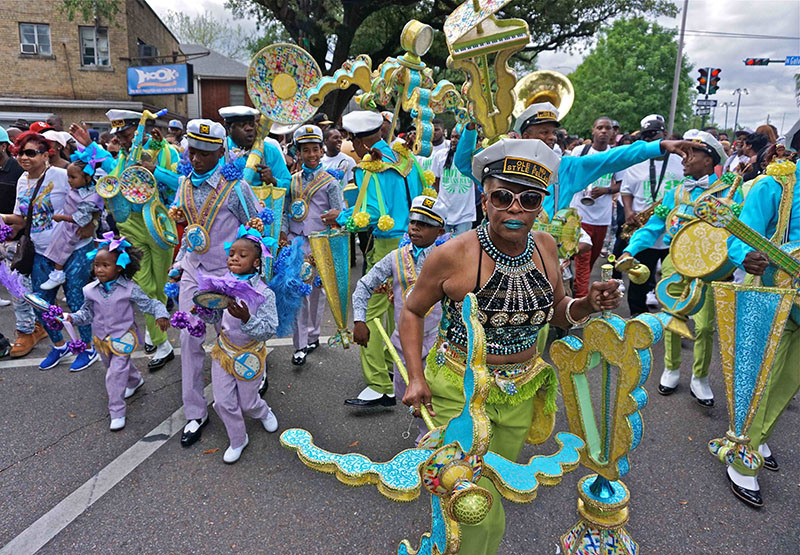 A vibrant parade scene with people dressed in elaborate, colorful costumes. They are playing musical instruments and marching down the street. The lively atmosphere is filled with energy and celebration.