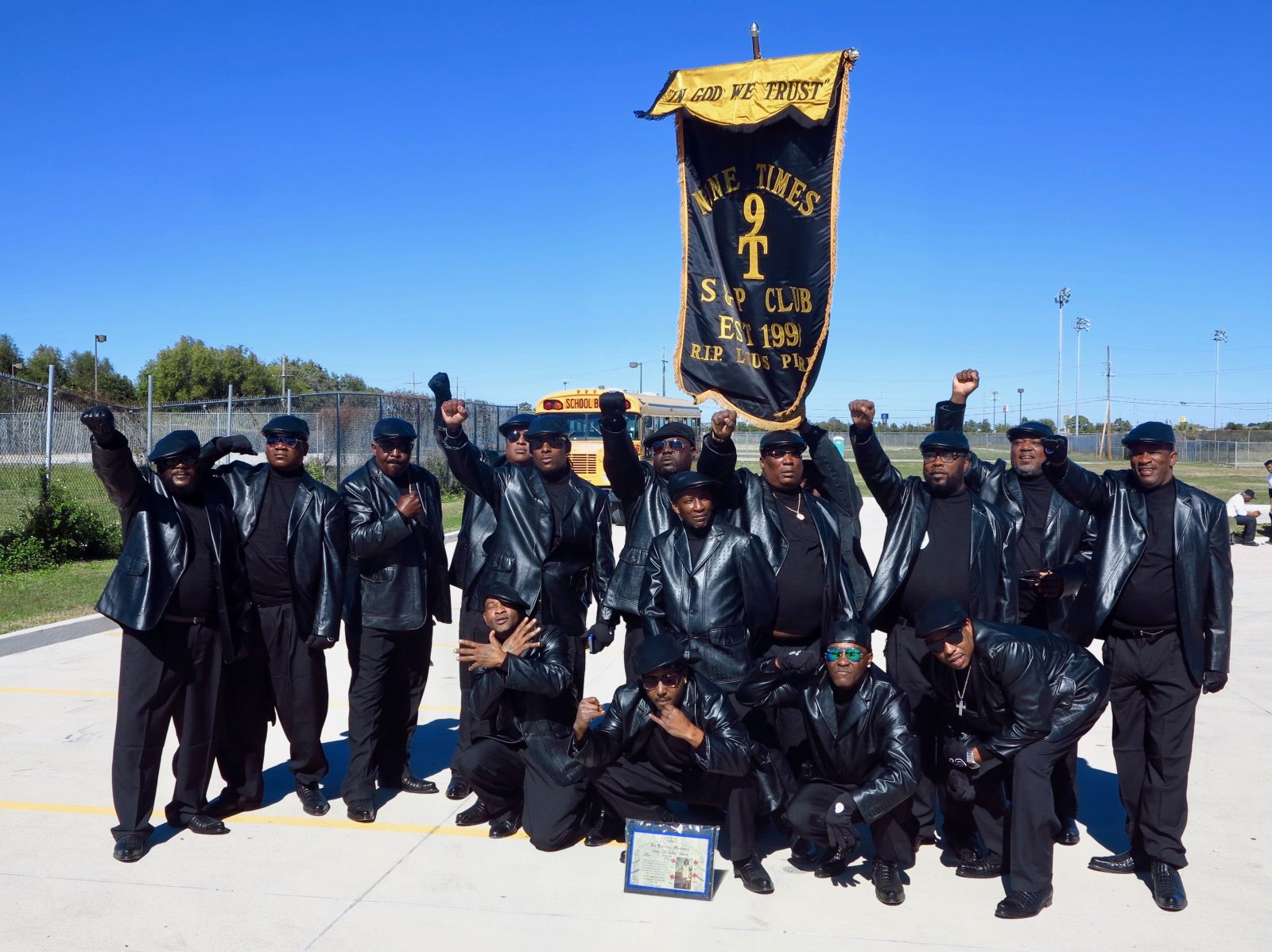 A group of men in black leather outfits and berets pose together, raising fists, with a banner reading "Nine Times S&P Club."