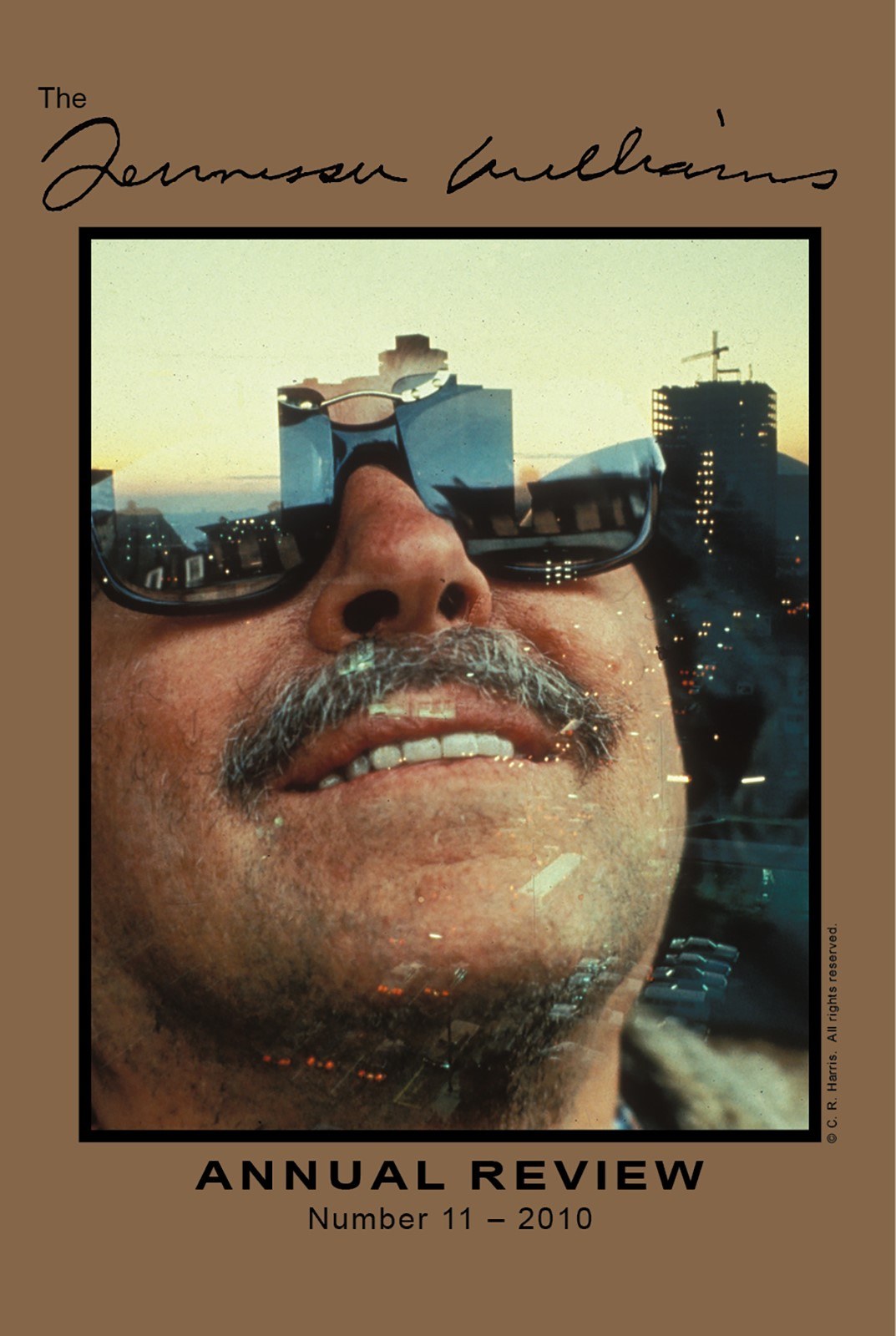 A man with sunglasses and a mustache smiles, with a cityscape reflected in his lenses. The cover is titled Annual Review Number 11 - 2010 with a signature at the top against a brown background.