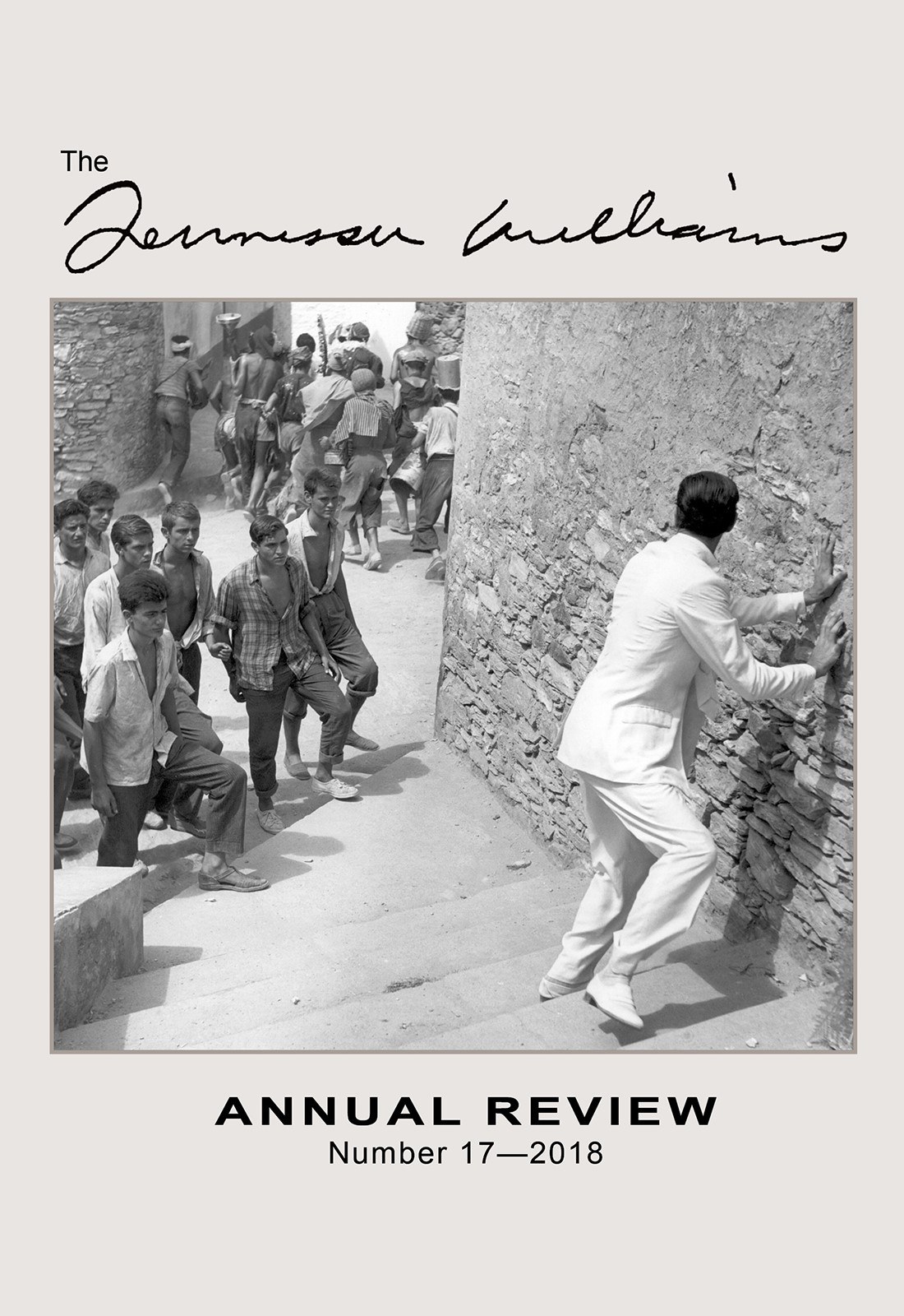A photograph of a man in a white suit climbing a stone wall, watched by a group of boys and young men in casual attire in a narrow alley. The image is part of the Tennessee Williams Annual Review, Number 17—2018.