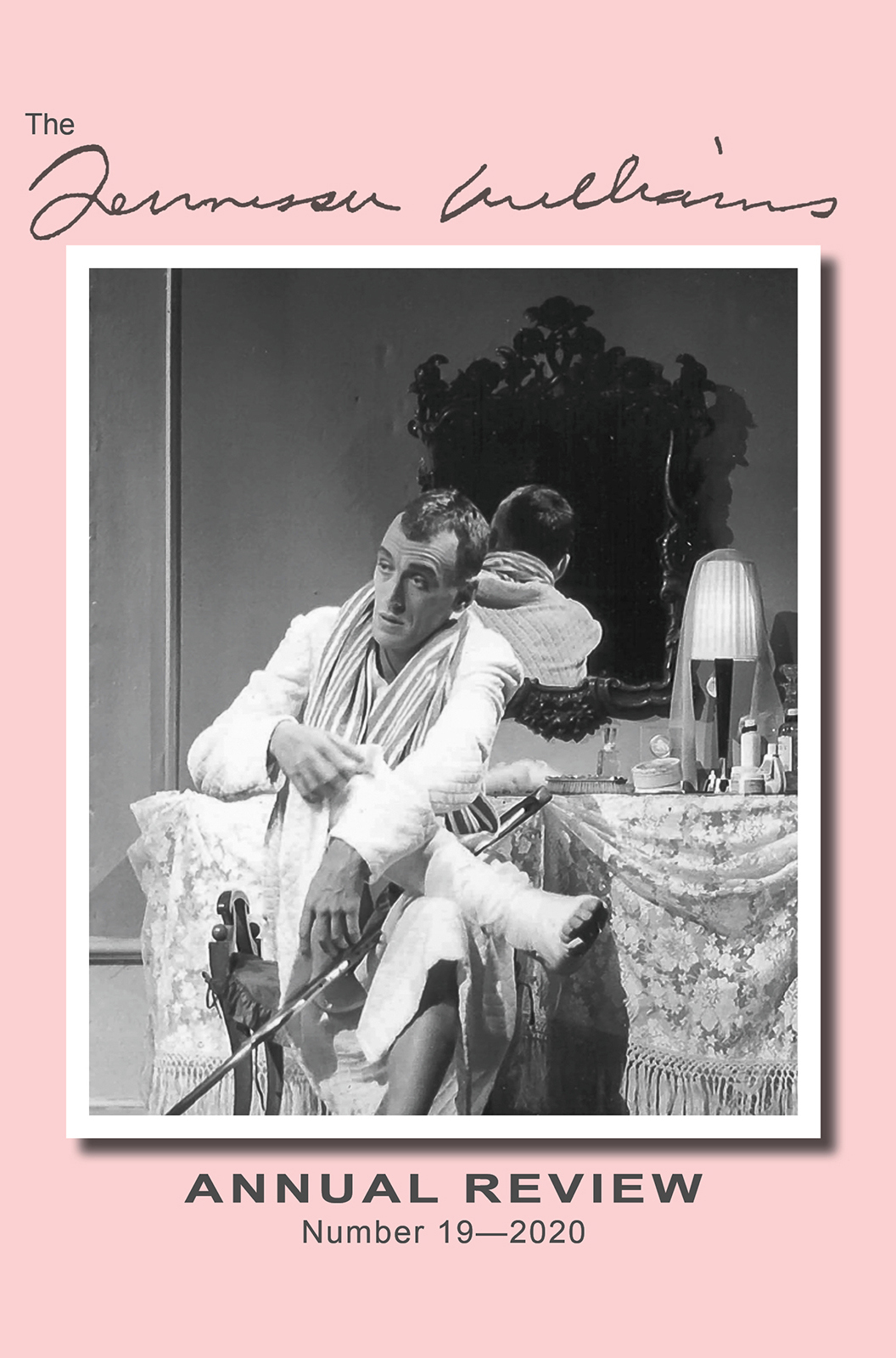A man sits in front of a mirror, dressing with a scarf and holding a shoe. The scene includes a vanity table with a lamp and various items, set against a pink background. Text reads The Tennessee Williams Annual Review Number 19—2020.