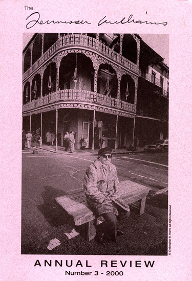 Black and white image of a person wearing a coat and hat sitting on a bench in front of a historic building with balconies. The text at the bottom reads Annual Review Number 3 - 2000.