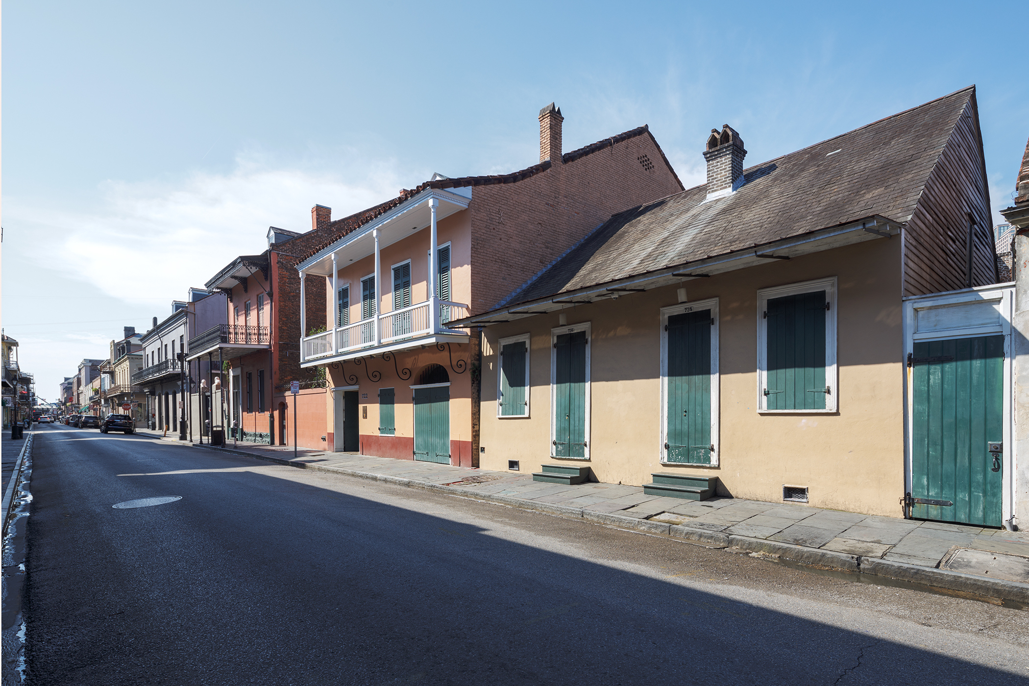 A view of a quiet street in the French Quarter of New Orleans, featuring rows of historic buildings with colorful facades and balconies under a clear blue sky.