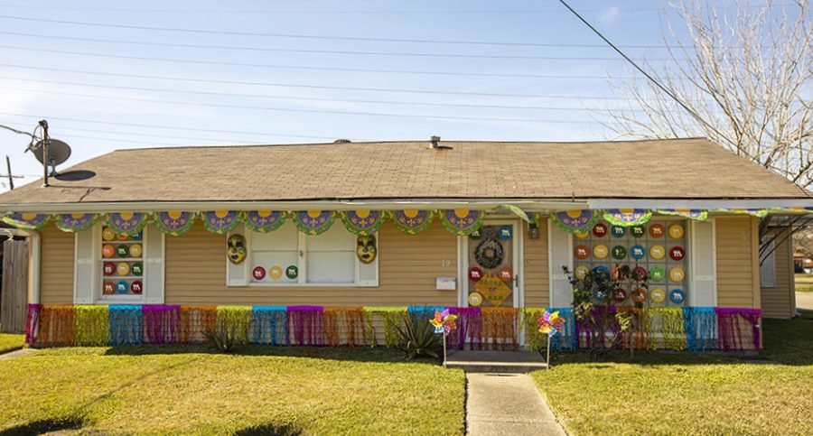 A single-story house is decorated for a celebration with colorful banners, masks, and wreaths. The front lawn is neatly trimmed, and a clear blue sky is overhead.
