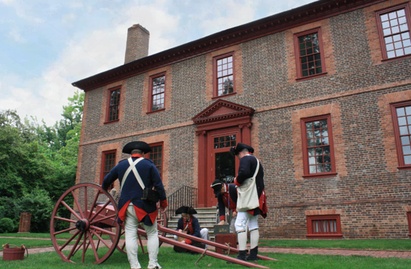A modern day photo of the Wilton House Museum, with a cannon and two men dressed as Revolutionary War era soldiers in front.