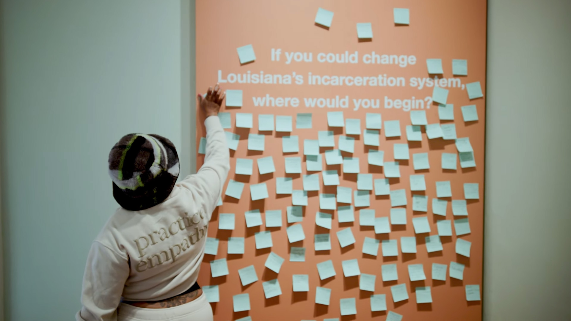 A screenshot from the video “Does Mass Incarceration Make Us Safer?” shows a woman adding a post-it note to a wall of post-it notes that answer the prompt "If you could change Louisiana's incarceration system, where would you begin?"