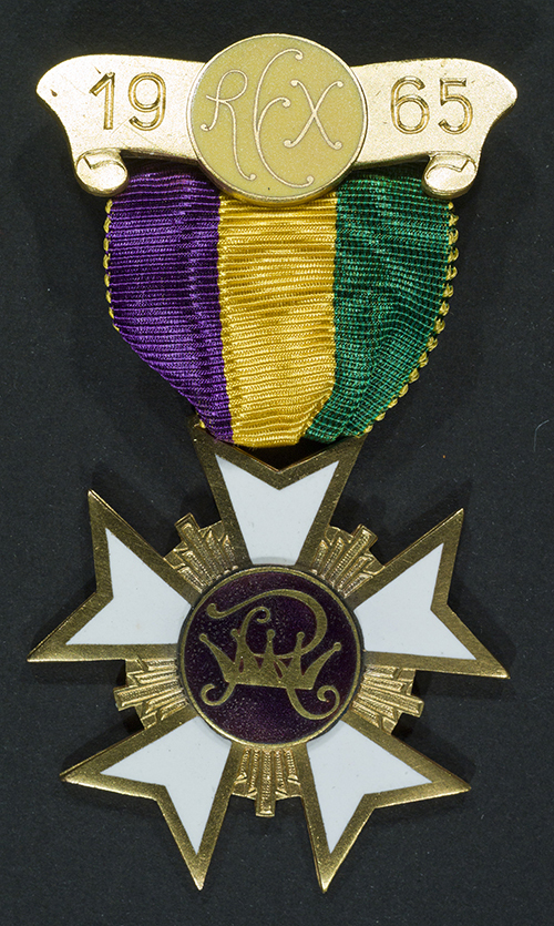A gold medal featuring a purple and green ribbon is attached to a star-shaped emblem with white and gold details. The top part reads 1965 and has decorative initials RFX.