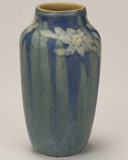 A tall, cylindrical ceramic vase featuring a blue glaze with soft vertical stripes and subtle floral patterns near the top. It has a smooth finish and rounded opening.