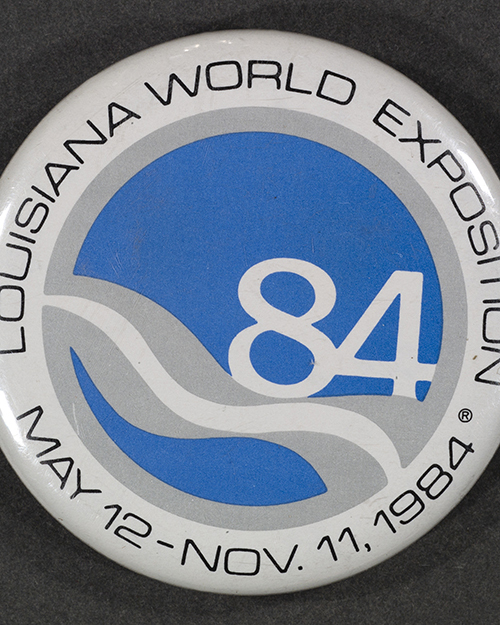 Button from the Louisiana World Exposition featuring the events logo. It displays a blue and gray design with the number 84 and the dates May 12 - Nov. 11, 1984.