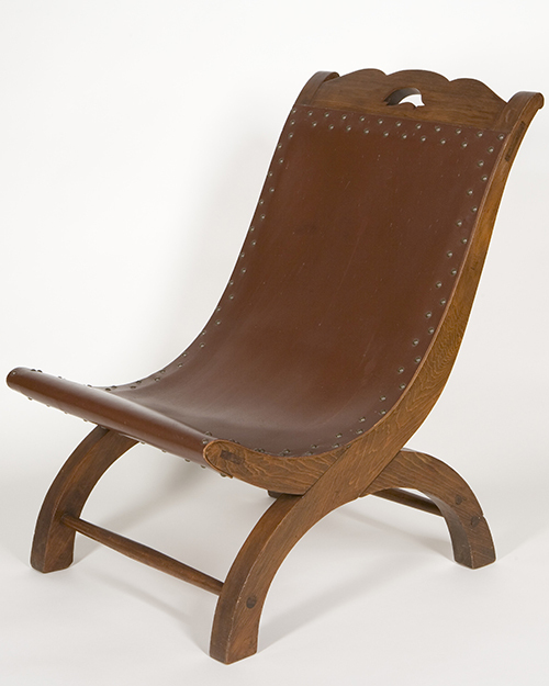 A vintage wooden chair with a curved leather seat and decorative studs. The frame has elegantly arched legs and a small, carved handle at the top. The design is simple yet stylish, showcasing craftsmanship.