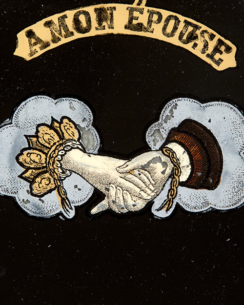 Illustration of two hands shaking, one adorned with flowers, the other in a suit, encircled by blue clouds. Above them is a banner with the text À MON ÉPOUSE. The background is black, creating a vintage, decorative appearance.