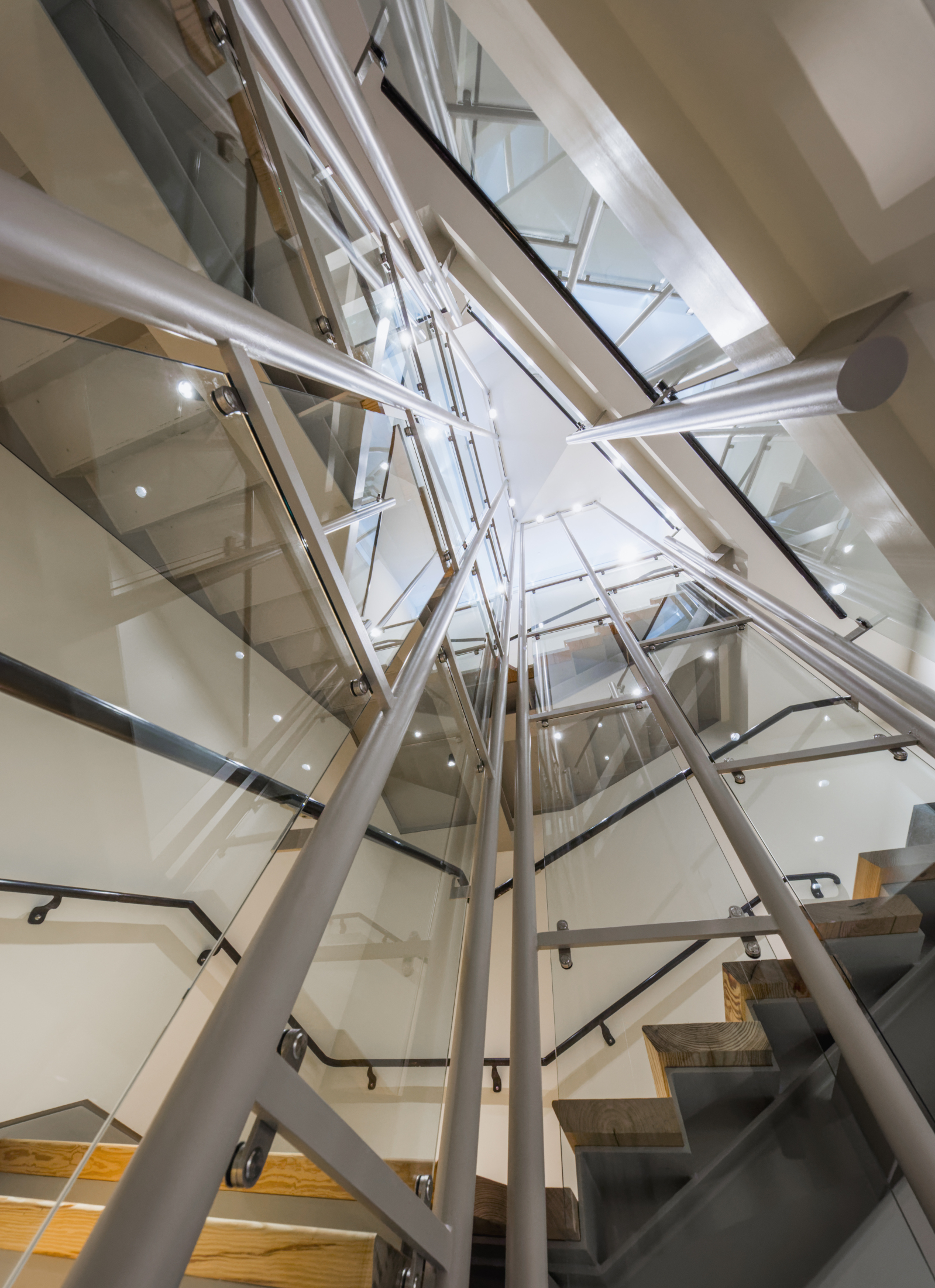 A modern, architectural staircase with sleek metal railings and glass panels, viewed from below. The design features multiple levels and sharp angles, creating a geometric and dynamic visual effect.
