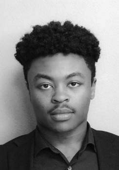 A black and white portrait of a person with curly hair wearing a dark shirt and blazer, looking directly at the camera with a neutral expression.