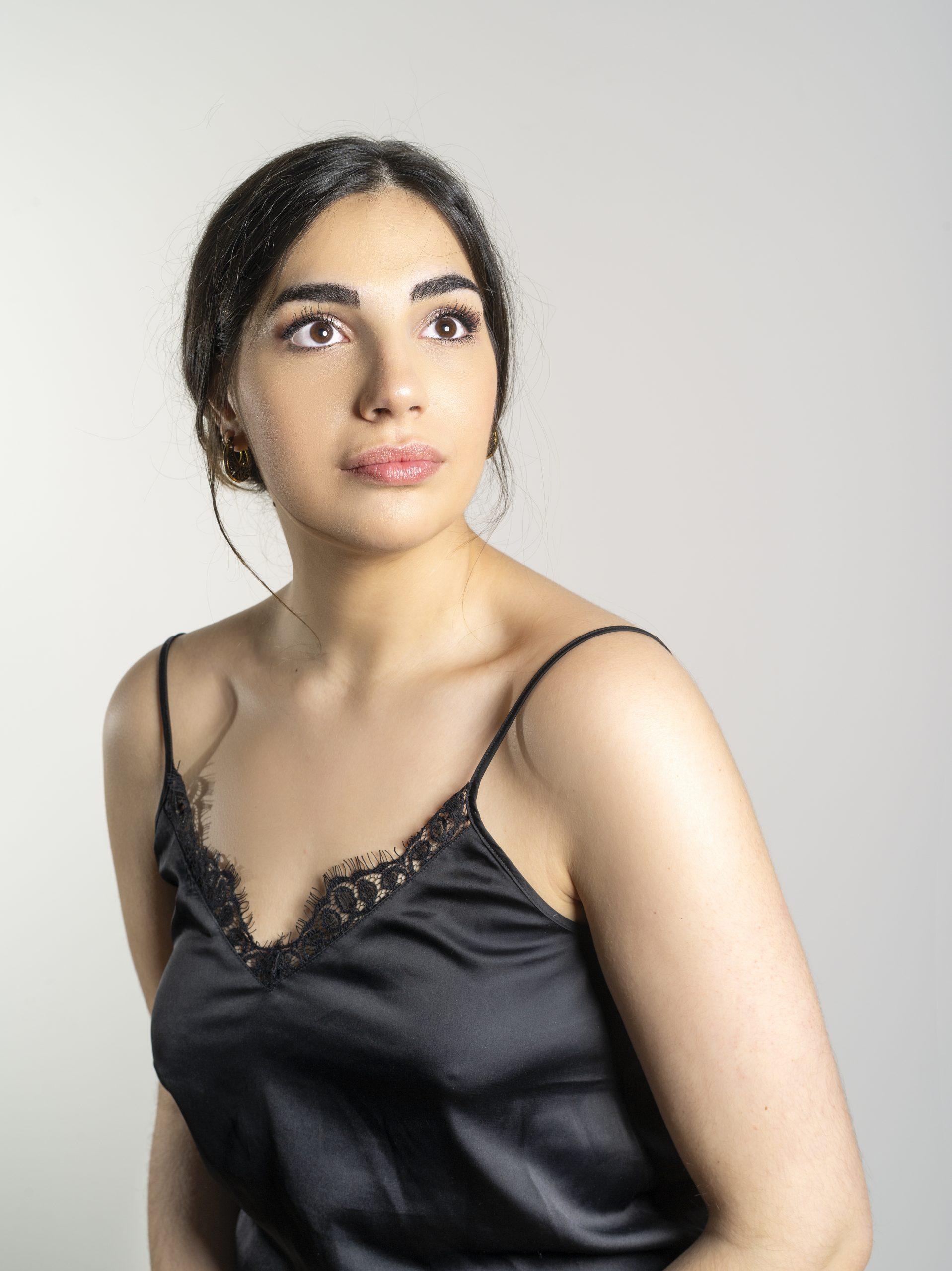 A woman with long dark hair, wearing a black lace-trimmed camisole, is looking upwards. She is against a plain, light background.