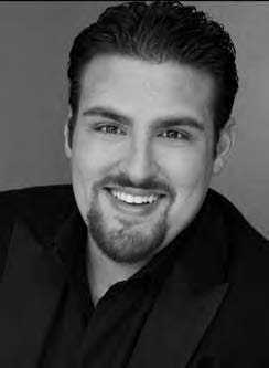 A black and white portrait of a man with short dark hair and a goatee, smiling at the camera. He is wearing a dark jacket over a collared shirt.