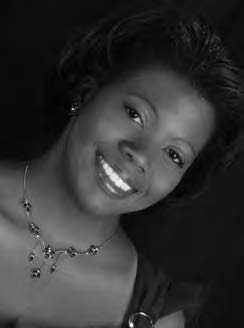 A woman with short dark hair is smiling at the camera. She is wearing a dark top and a necklace, and the image is in black and white.