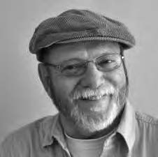 A smiling man with a beard and glasses is wearing a flat cap and a button-up shirt. The image is in black and white.