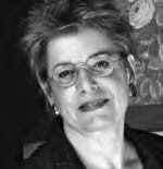 Black and white portrait of a person with short hair and glasses, smiling softly. They are wearing a dark blazer and earrings. A patterned background is partially visible.