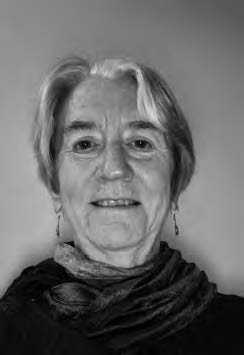 Black and white portrait of an older person with short hair, smiling softly. They are wearing earrings and a dark scarf, and the background is a plain grey.