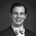 Black and white portrait of a man in a suit and bow tie, smiling at the camera.