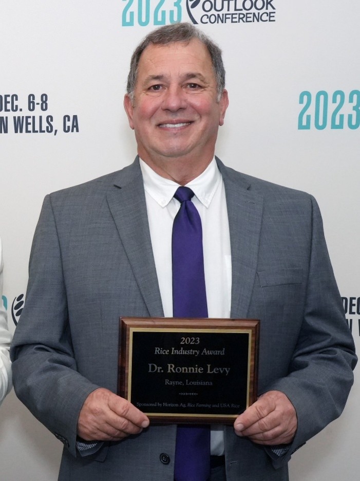 Headshot for Ron Levy. He is pictured in a suit holding an award plaque.