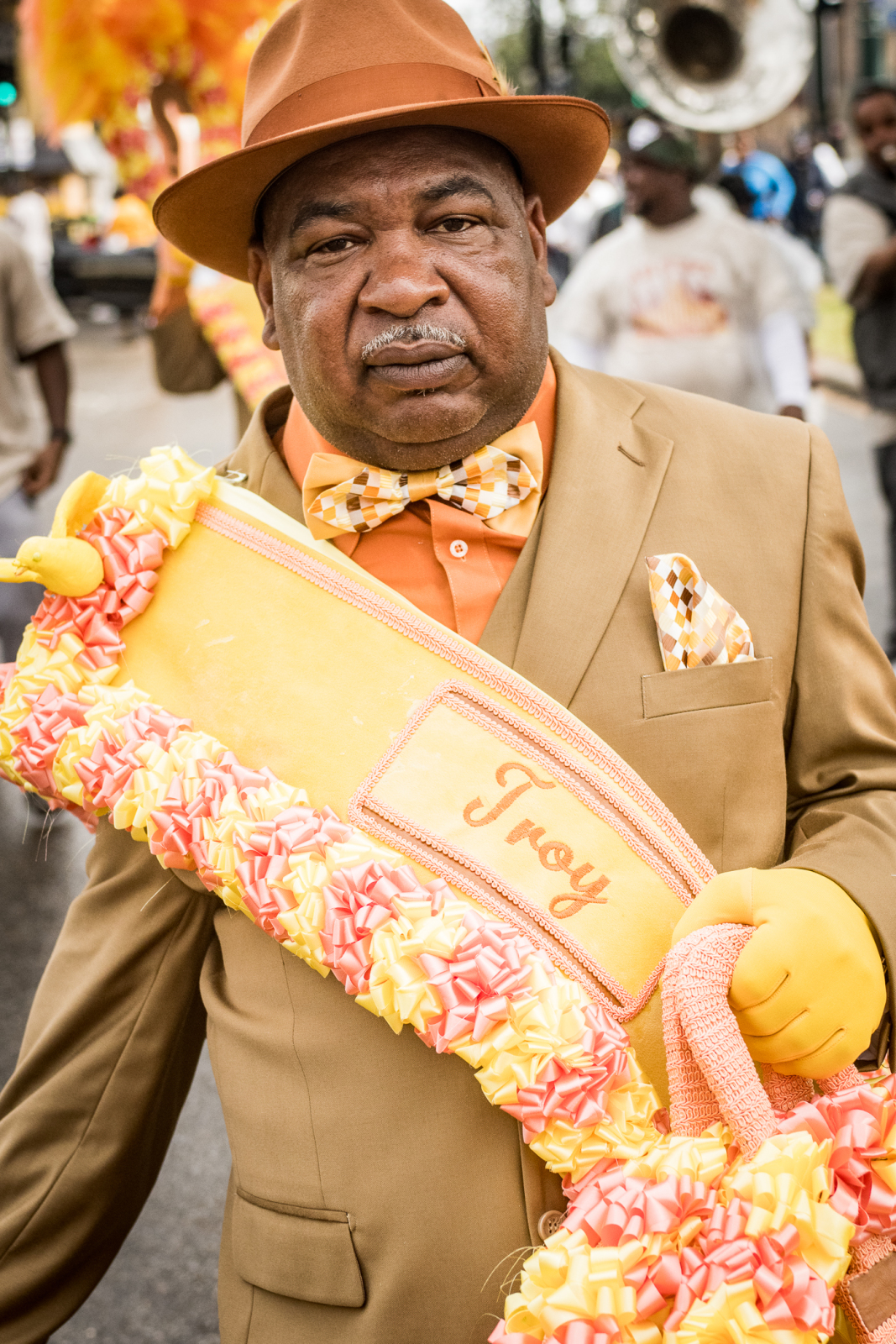 Troy Materre of ? Mark Social Aid and Pleasure Club poses for a photo. He's wearing a lime green jacket, yellow sash with decorative flowers, and a matching hat.