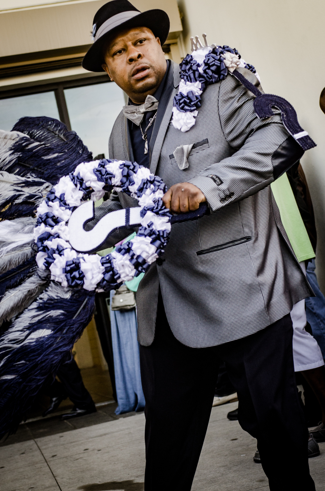 Mark Lewis of ? Mark social aid and pleasure club wears a patterned jacket with purple flourishes and matching hat, while carrying a question mark-adorned parade fan.