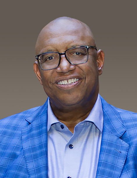 A person smiling, wearing glasses and a blue plaid blazer over a light blue shirt, set against a plain background.
