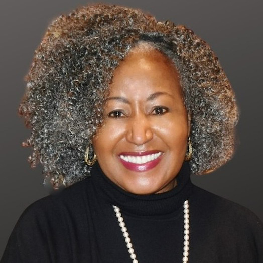 Smiling woman with curly gray hair, wearing a black turtleneck and pearl necklace, set against a plain dark background.