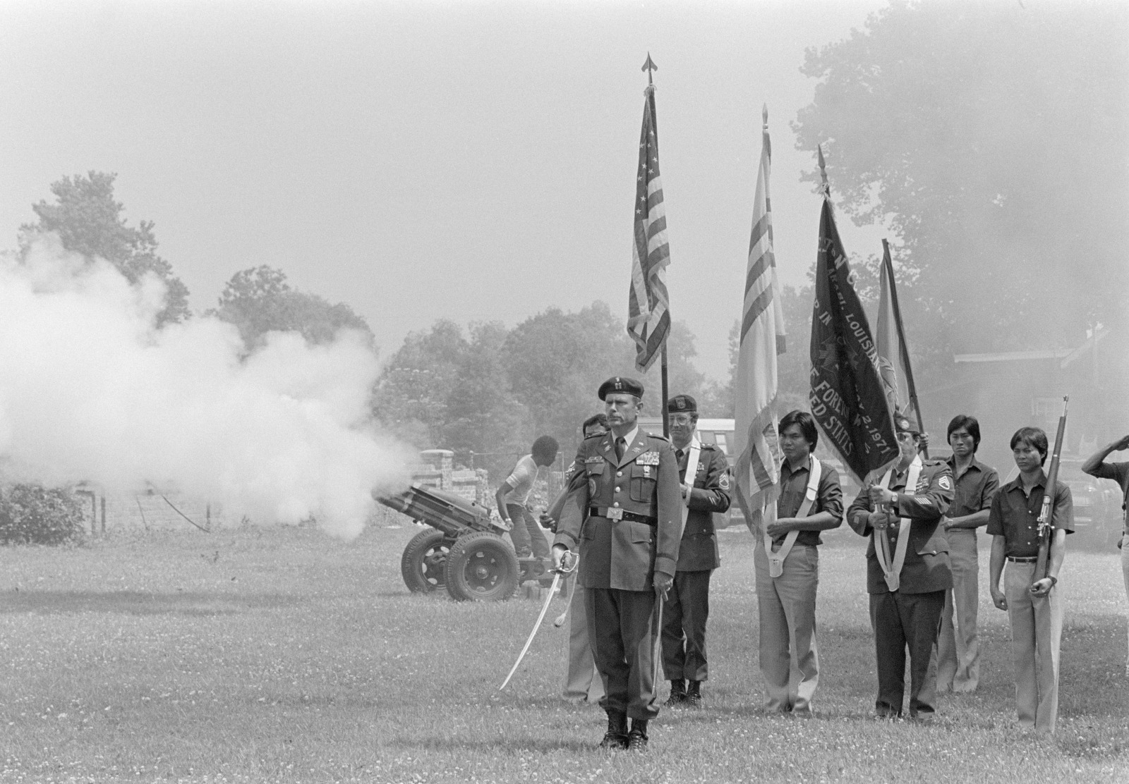 A black and white photo shows a joint Vietnamese and American color guard saluting US soldiers killed during the Vietnam War.