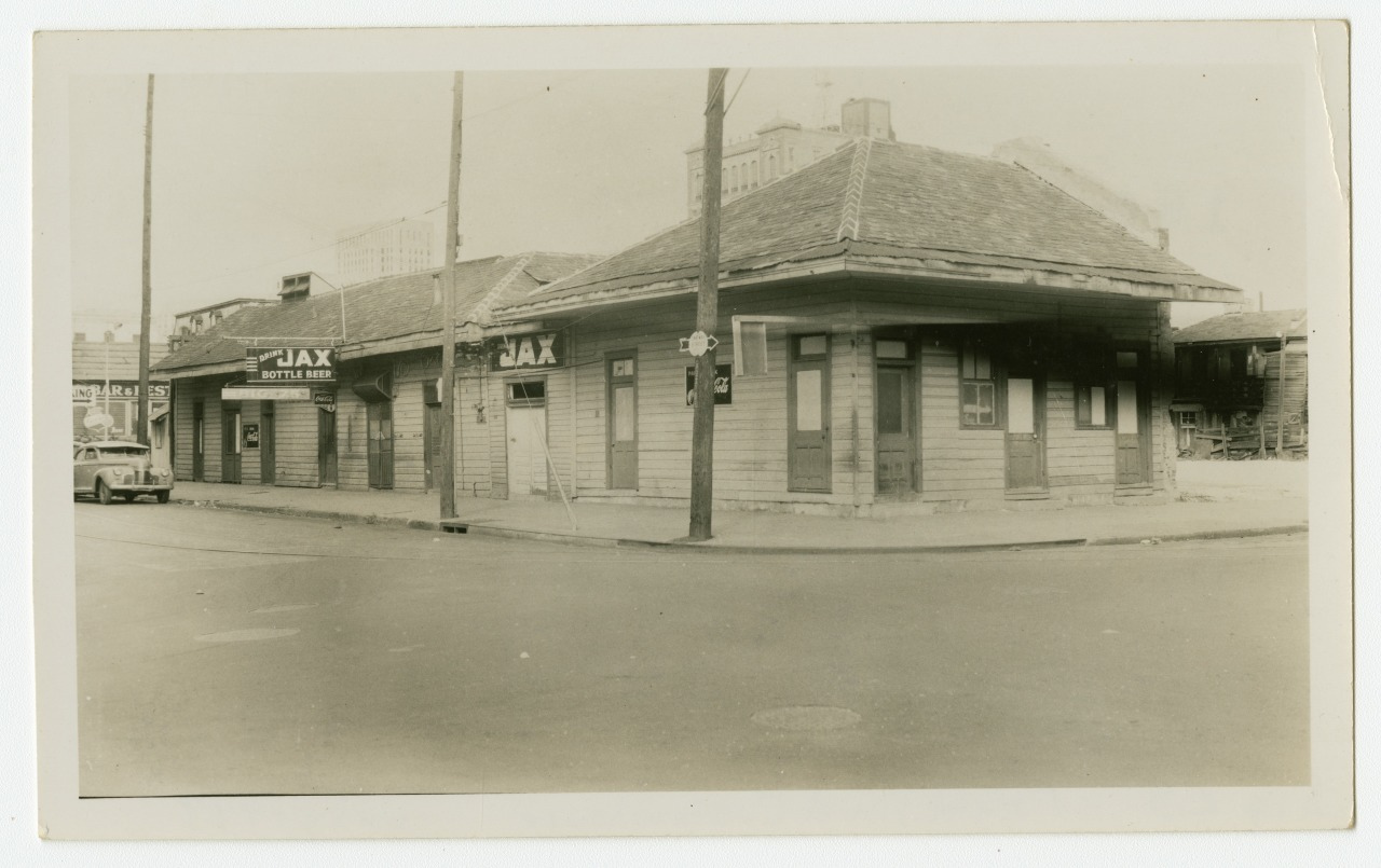 A vintage black and white photo of a corner building with signs reading JAX BREWERY and JAX in large letters. The structure features wooden siding and a shingled roof, with a quiet street in the foreground.
