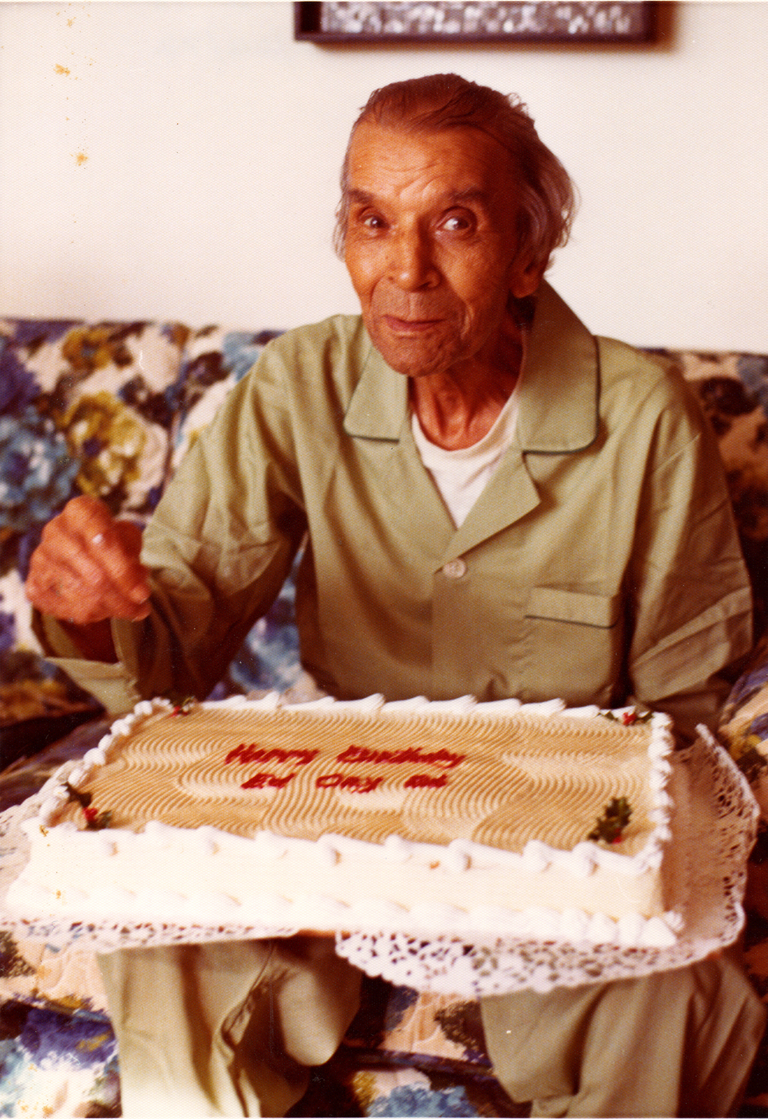 A vintage color photo shows an elderly Kid Ory holding a birthday cake.