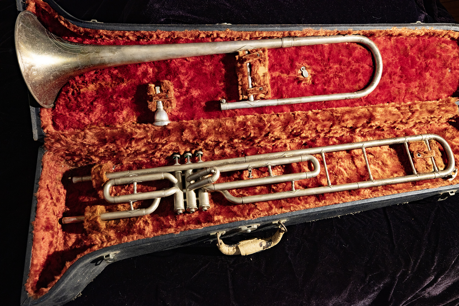 A valved trombone sitting in its red velvet-lined case.