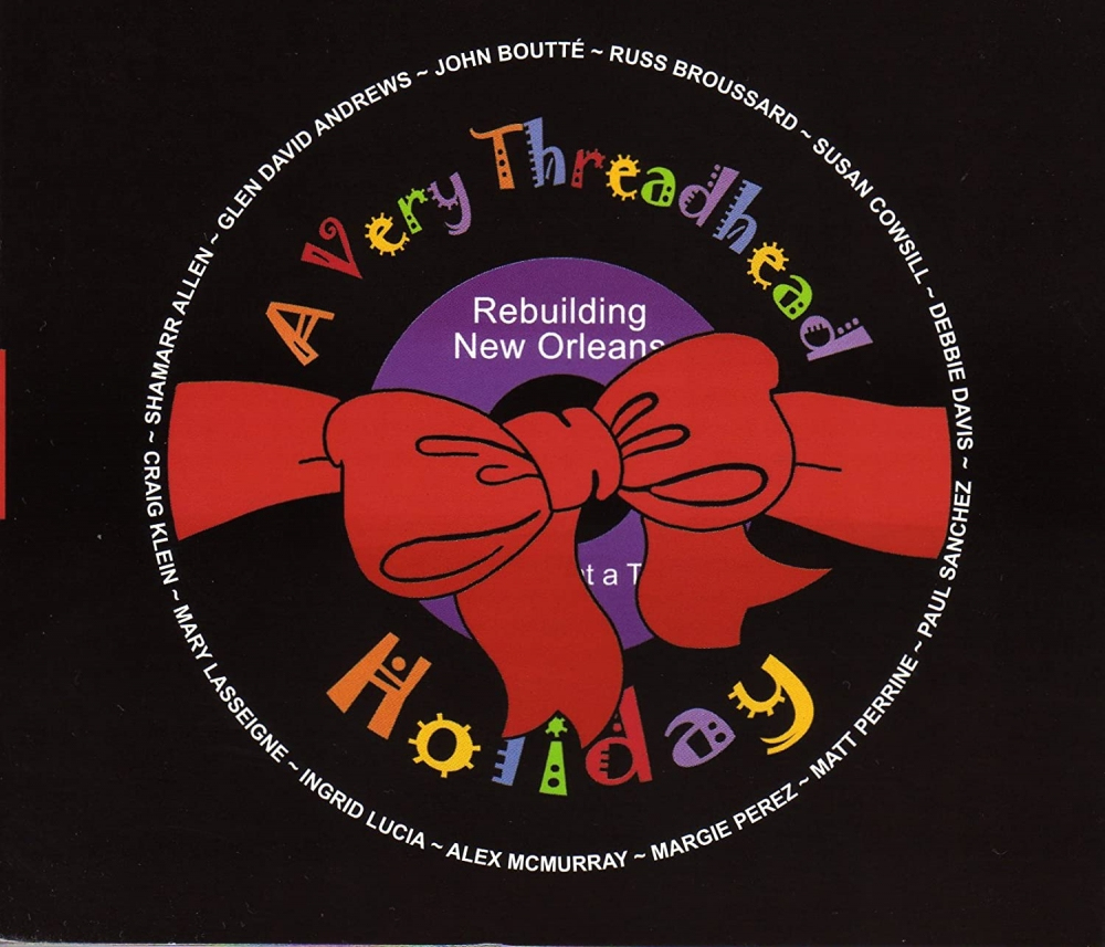 A circular design with a red bow in the center. The text reads A Very Threadhead Holiday and Rebuilding New Orleans along with names of various artists around the circle. The background is black.