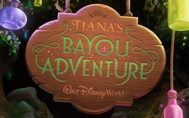A wooden sign with the text Tianas Bayou Adventure and Walt Disney World hangs among colorful lanterns in a lush, green environment. The letters are in a bright green and gold font.