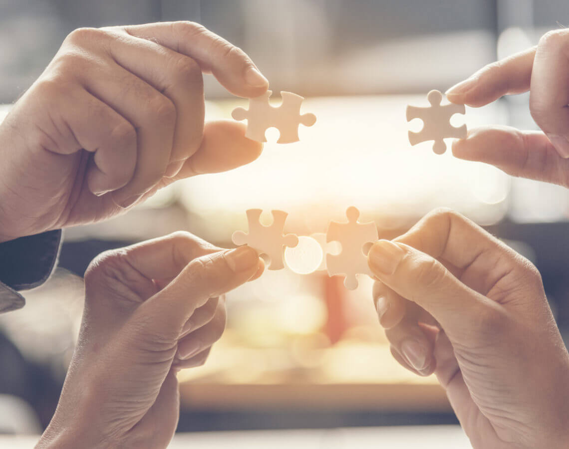 4 hands showing puzzle pieces coming together