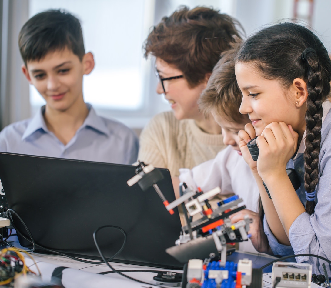 K-12 students and teacher working on laptop with robotics school
