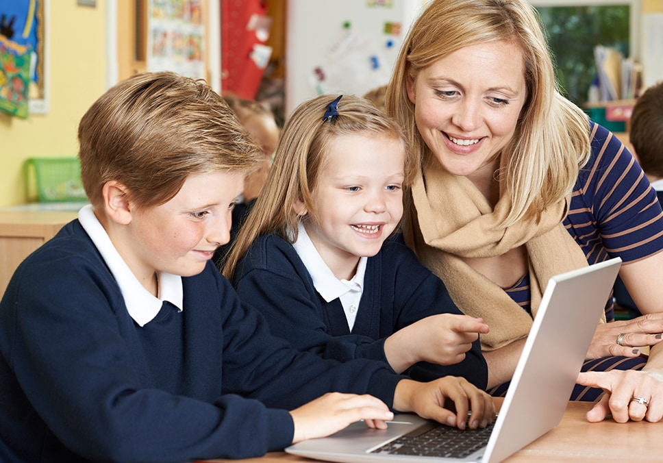 Teacher helping two K-12 school students on a laptop
