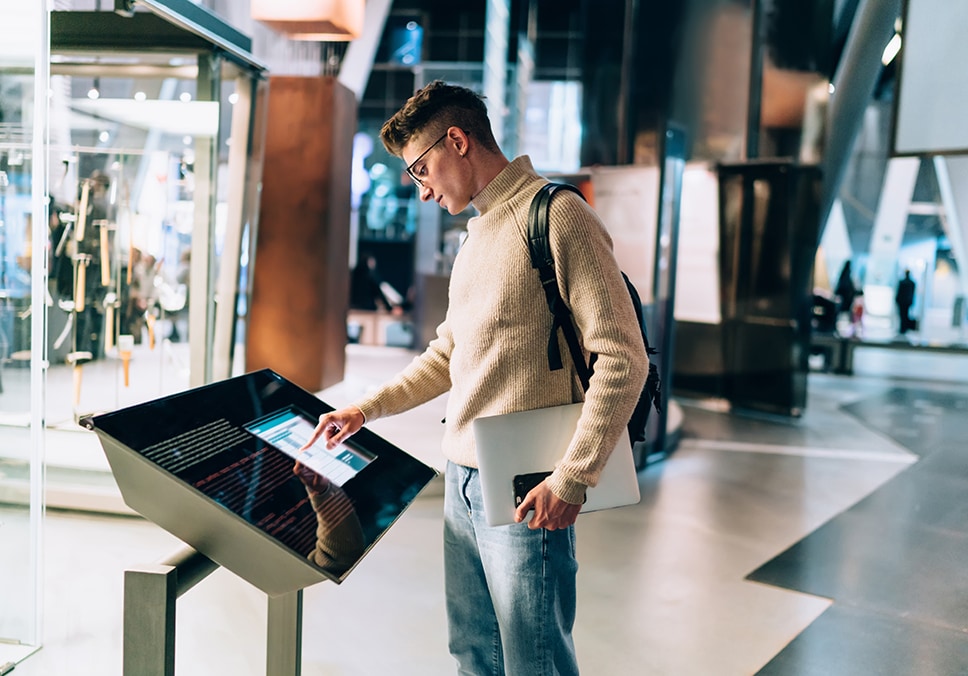 Man with laptop and phone using an interactive display at a museum