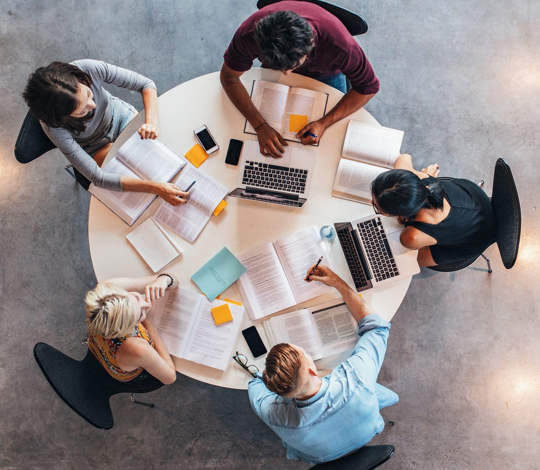Students collaborating on a table with laptops and devices